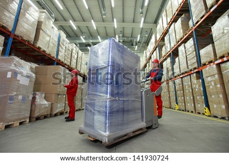 warehousing - management of the flow of resources - two workers in uniforms and safety helmets working in storehouse