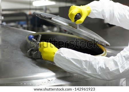 hands in yellow gloves opening industrial process tank - close up
