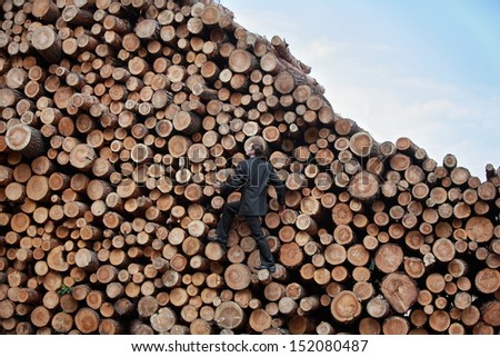 Young business man on his way to the top of the large pile of cut wooden logs