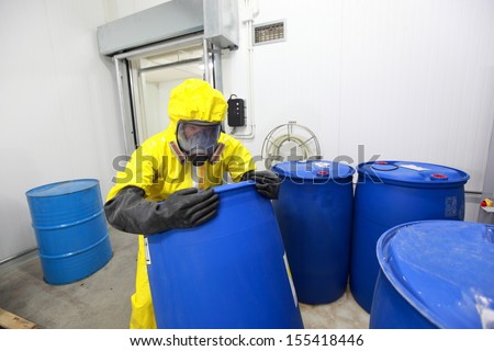 risky job - technician in protective uniform rolling barrel with toxic substance in plant