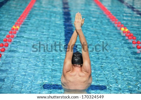 swimmer in cap raising hands, preparing to swim in sunny blue water swimming pool - back view