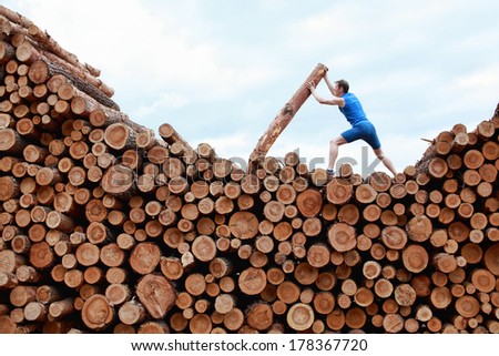 man on top of large pile of logs, pushing heavy log - training
