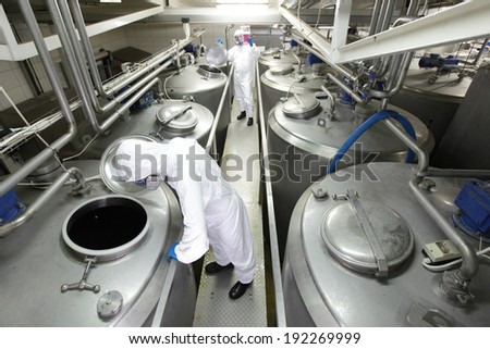 Two workers in white protective uniforms,mask and goggles working with industrial process tanks in plant