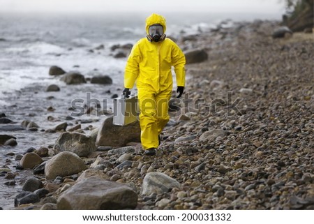 specialist in protective suit with silver suitcase walking on rocky beach in stormy day