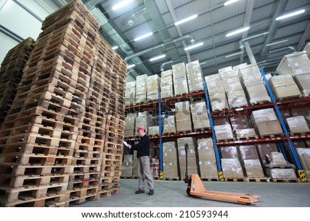worker with hand pallet truck preparing delivery - stack of wooden pallets in storehouse