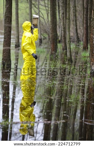 fully protected in uniform,boots,glove s and mask technician examining sample of water in plastic container in floods area