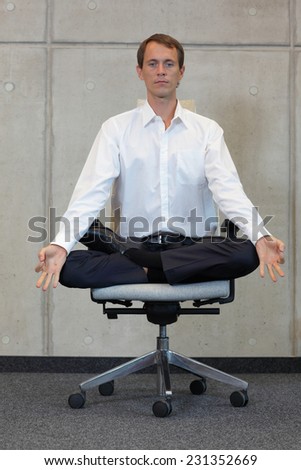 meditating caucasian businessman in lotus pose on office chair
