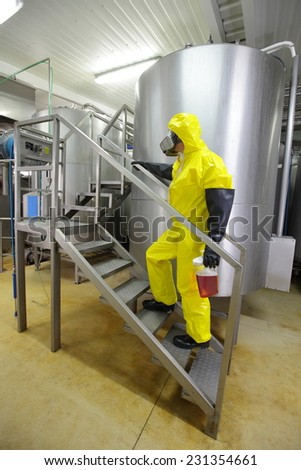 technician in protective coveralls with sample of fluid in plastic container walking up the stairs in laboratory