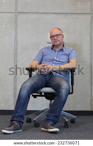 middle age balding man with eyeglasses bad sitting position on chair in office - front view