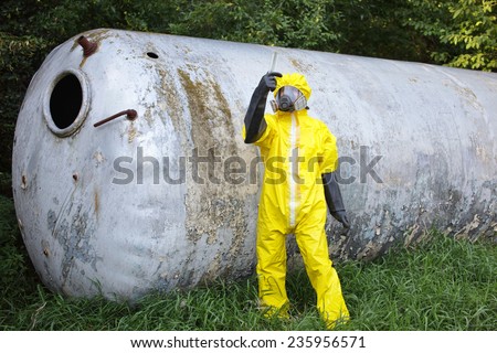 contamination - technician in protective coveralls ,mask, and gloves examining sample from large stainless tank