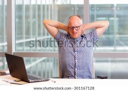 middle age balding man with pain in the neck stretching arms in his office