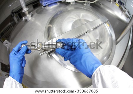 hands in blue gloves opening industrial process tank