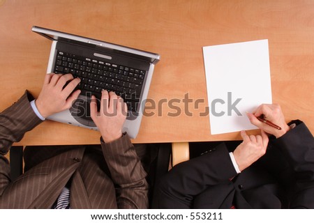 2 men working on laptop and writing on a paper  at the desk in the office - close up