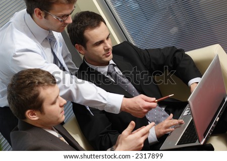 Three business men working together on laptop in the office. one is standing two are sitting on leather sofa - close up