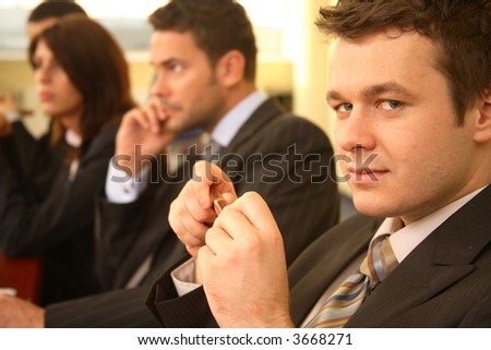 Group of business persons in suits sitting at a conference table, taking part in a meeting and/or presentation - one man in focus, portrait
