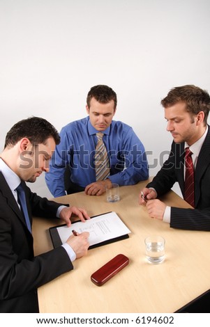 Three businessmen sitting at a table negotiating and signing a contract.