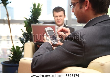 two young business men siting on leather sofa and working at laptop and palmtop in the office
