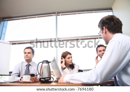 A group of four business people gather around a conference room table for a working discussion to plan a new project.