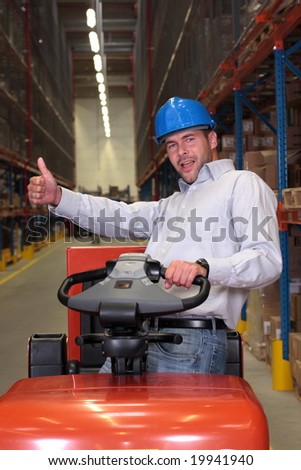 A male warehouse worker, driving a small forklift in the warehouse.