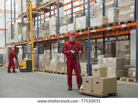 Two workers in uniforms and safety helmets working in storehouse Two workers in uniforms and safety helmets working in storehouse