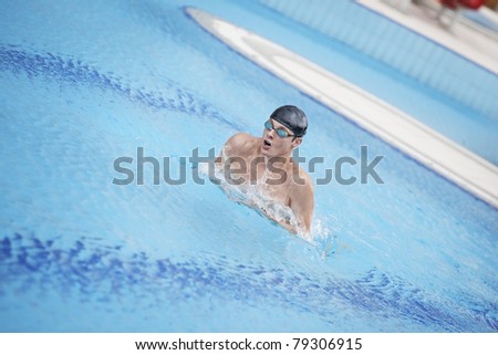 Swimmer in cap and goggles taking breath in swimming pool,raising head and torso out of the water