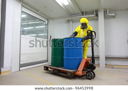 Worker in protective uniform,mask,gloves and boots  working with barrels of chemicals on forklift