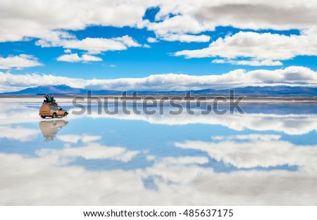 Car with happy people driving on the mirror surface of Salar de Uyuni in Bolivia with clouds reflection