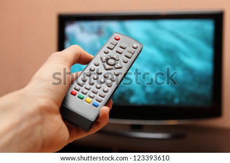 Hand holding TV remote control with a television in the background