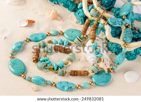 Turquoise necklace lying on white sand with sea-shells
