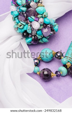 Turquoise necklace and bracelet lying purple background with white scarf