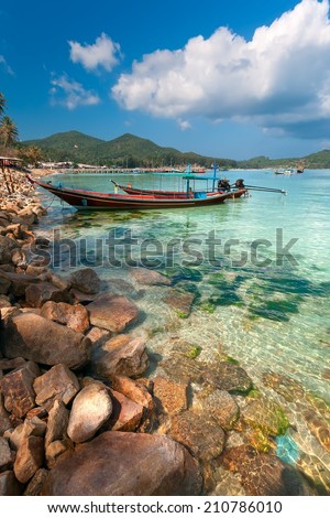 the wooden fishing boat on the stone coast with transparent water