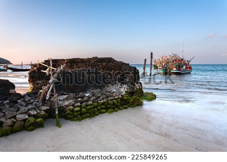 sunset on the coast with fishing boats and the destroyed stone wall.