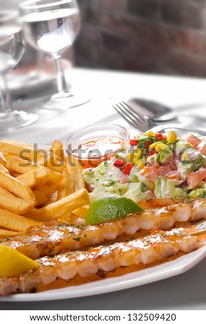 Grilled Shrimps served with french fries and fresh salad. Selective focus on shrimps.