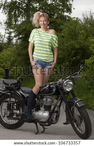 Young woman in sexy outfit stands on an old motorcycle / Old and Young