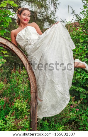 Beautiful bride in her wedding gown posing in a lush green garden with a joyful smile on her face / Beautiful bride in her wedding gown