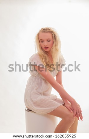 Beautiful innocent young woman with long blond hair sitting demurely with her hands folded and downcast eyes / Beautiful innocent young woman