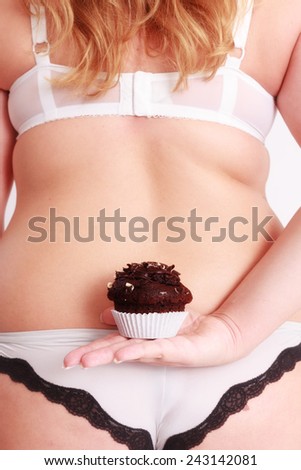 Fat woman dressed in lingerie holding a chocolate muffin behind his back in his hand / Fat woman holding a muffin behind his back in his hand