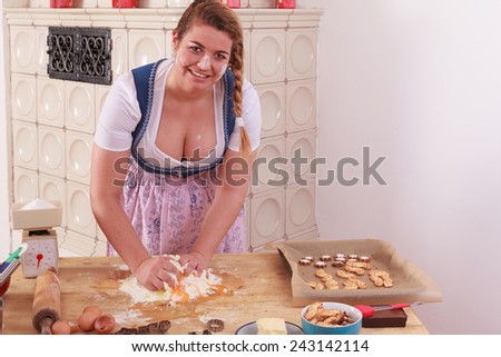 Young Bavarian woman in dirndl with deep neckline kneads the dough has flour on her face and chest - landscape orientation / Young woman with deep cleavage kneads dough and has flour on her face