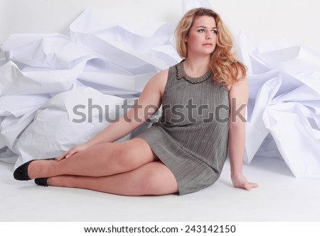 Size Full length portrait of a beautiful plus curly young blond woman posing on white in gray dress and pumps / Portrait of a beautiful plus size curly young blond woman