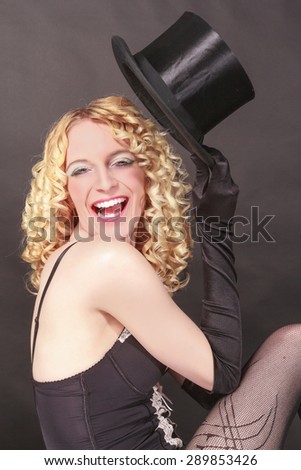Laughing young, blond, wavy woman in underwear lifts your top hat to the greeting with closed eyes. / Amusing woman with top hat