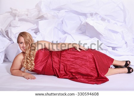 Beautiful blonde woman with oversize in an elegant dress and curly hair, lying on the ground in front of a paper hill.