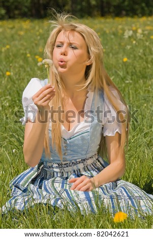Bavarian girl sitting in the grass with dandelion in his hand /Bavarian girl in the meadow