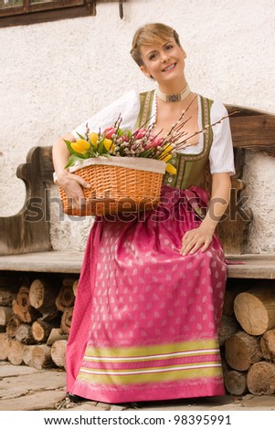 Bavarian girl sitting on a bench in dress and bouquet of Easter basket /Young girl with Easter bouquet Bavarian