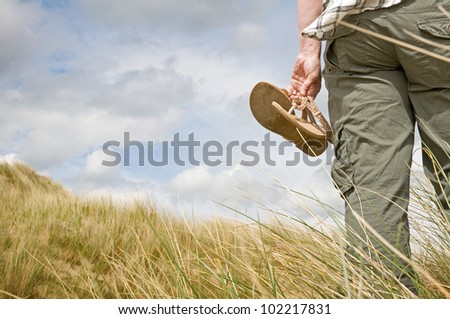 woman walking in sand dunes holding sandals