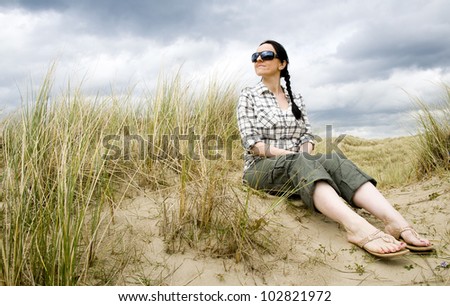woman sitting in sand dunes on beach with sun glasses on