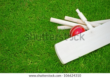 cricket set including ball, bat and stumps on green grass pitch with copy space