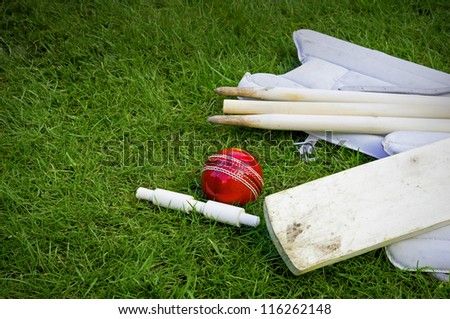 cricket ball, bat & pads with stumps and bail on grass