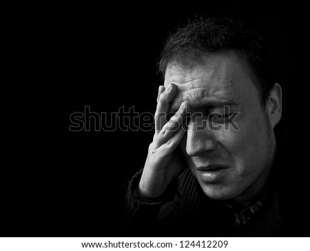 man feeling pain, frowning with hand on head with black background