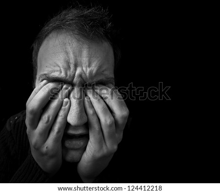 man feeling upset / in pain with fingers covering eyes on black background with copy space