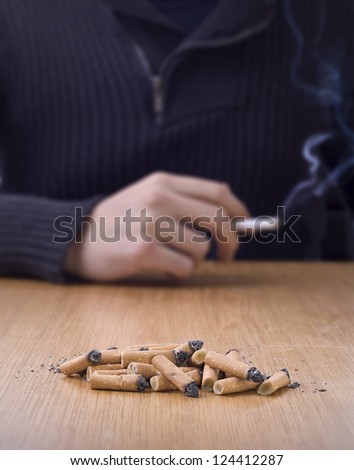 chain smoking, pile of cigarette butts on table with person smoking in background